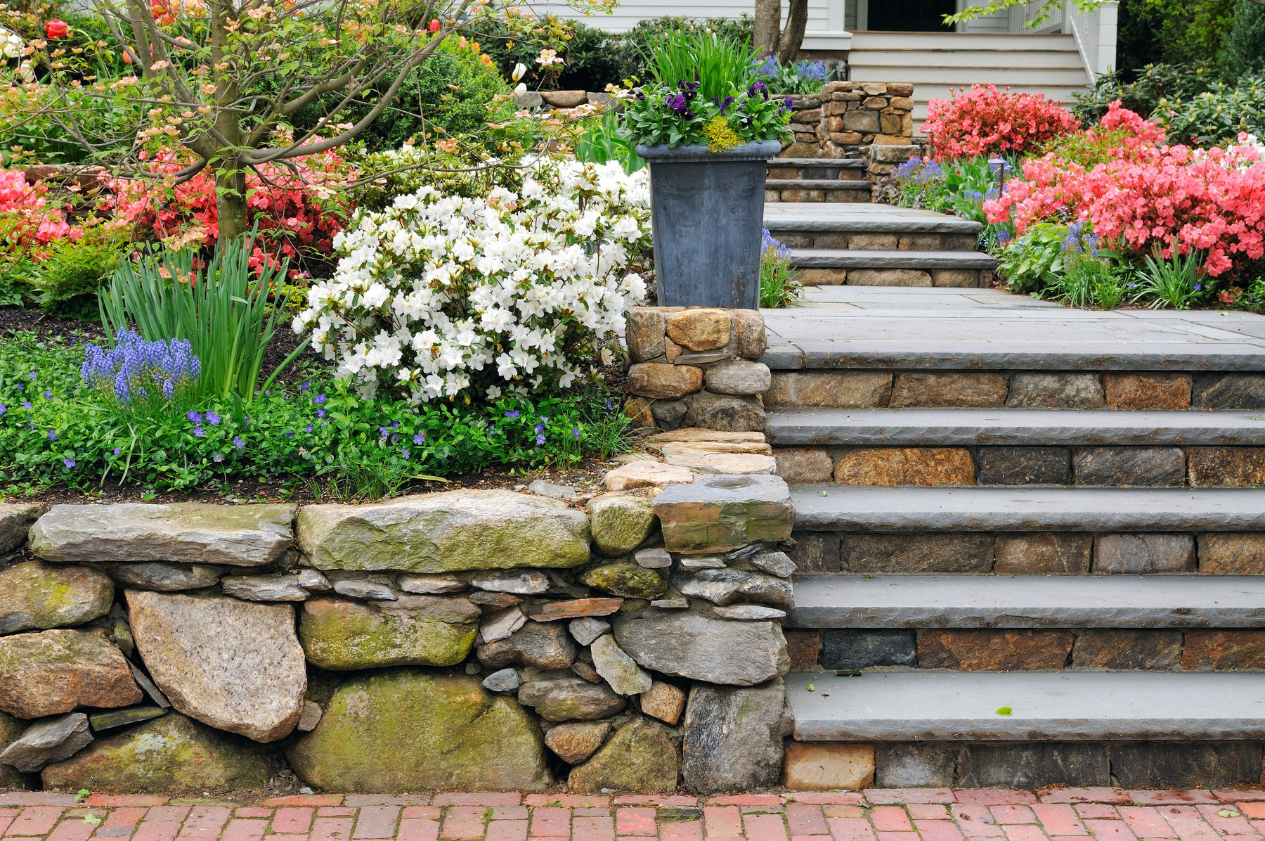 A picture of stone landscaping with stone steps, flowers and a paved walkway