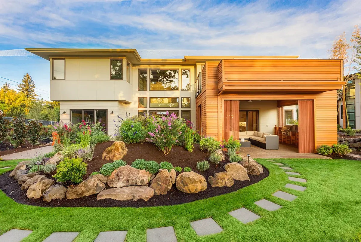 The exterior of a modern house with a well manicured and landscaped backyard with plants, rocks, grass and pavers