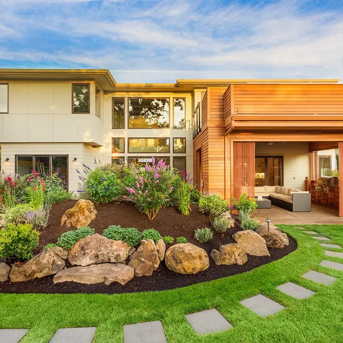 The exterior of a modern house with a well manicured and landscaped backyard with plants, rocks, grass and pavers