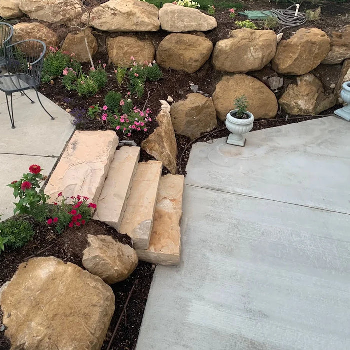 Outdoor garden area with stone wall, plants, and flowers on a concrete patio.