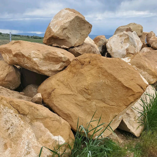 Large brown stones with grass in the foreground and a cloudy sky in the background
